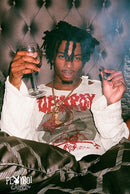 Person wearing a white sweatshirt with red text, holding a glass and a cigarette against a textured wall.