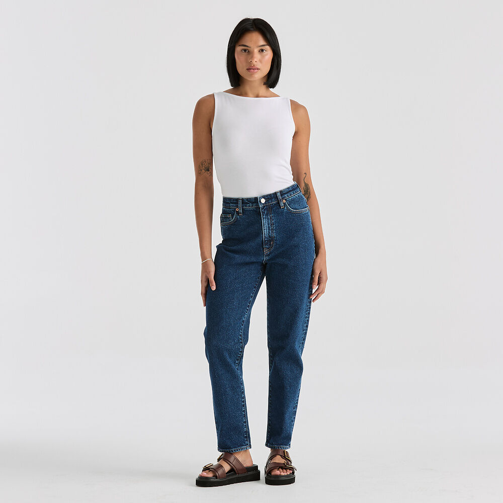 Woman wearing blue jeans and a white top on a plain background