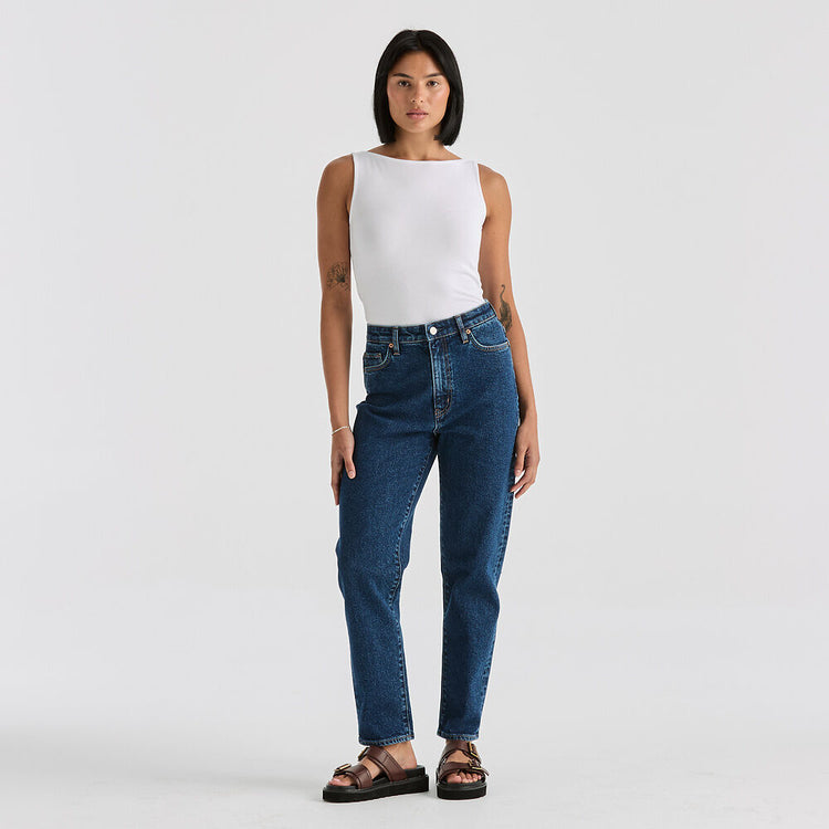 Woman wearing blue jeans and a white top on a plain background