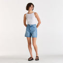 Woman wearing a white tank top and blue denim shorts on a white background