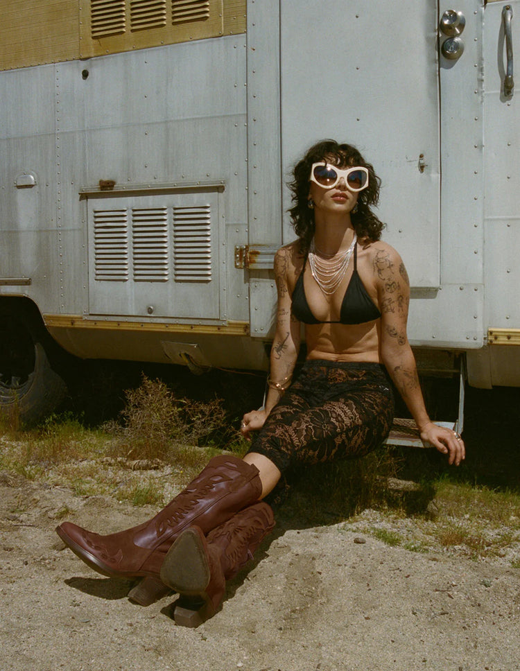 A person wearing a brown suede boot with a pointed toe and half zip feature, sitting in front of a mobile home.
