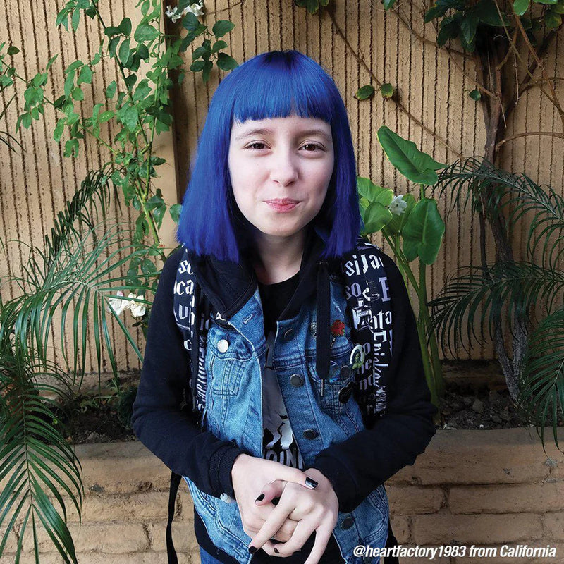 Person with blue hair standing outdoors with plants in the background