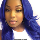 Person with vibrant blue hair wearing a white shirt, with a blurred background.