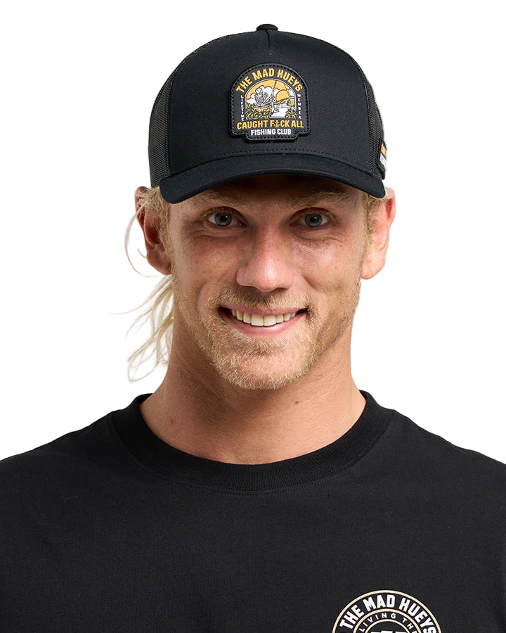 Man wearing a black cap with a logo and matching black shirt on a gray background