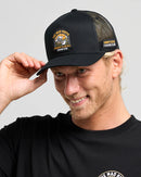 Man wearing a black cap with branding and a matching black shirt on a gray background