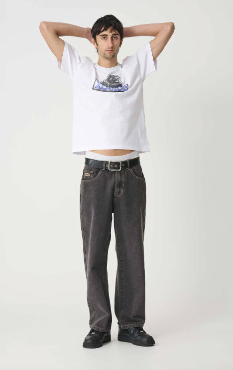 Person wearing a white t-shirt with a graphic design and dark jeans on a plain background