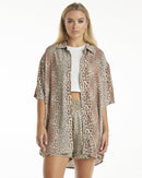 A female model wearing a leopard print shirt tied at the waist with shorts, posing against a neutral background.