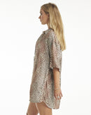 A female model wearing a leopard print shirt tied at the waist with shorts, posing against a neutral background.