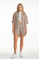 A female model wearing a leopard print shirt tied at the waist with shorts, posing against a neutral background.