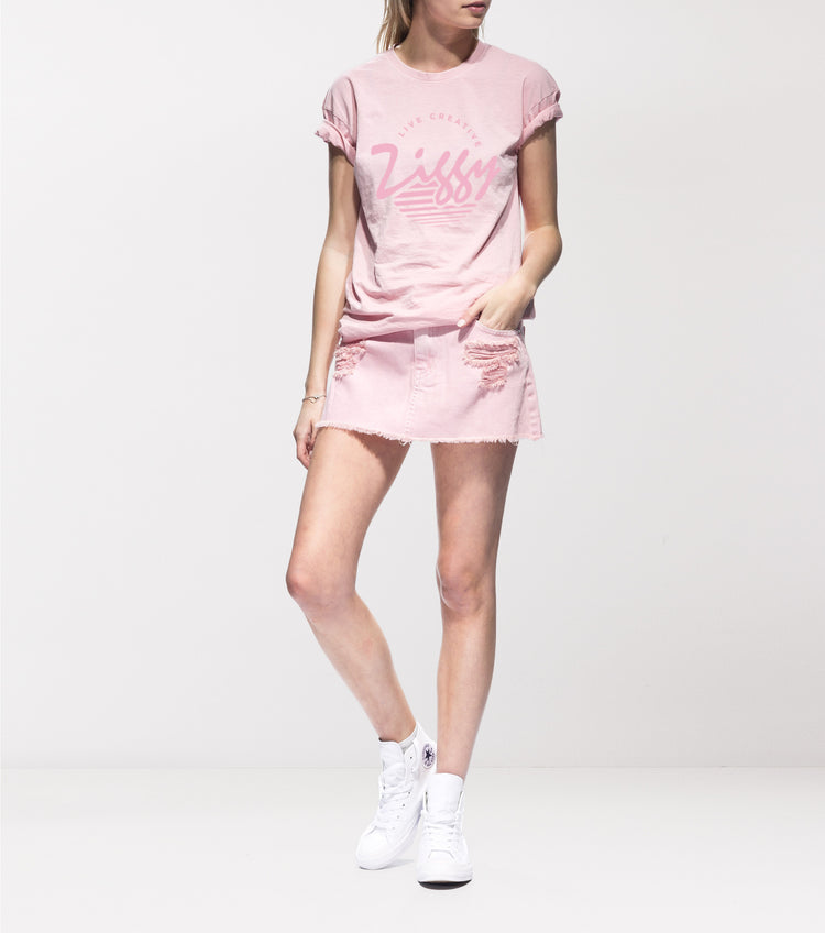 A female model wearing a pink t-shirt with the text 'ZIGGY' on it, paired with a matching pink denim skirt and white sneakers.