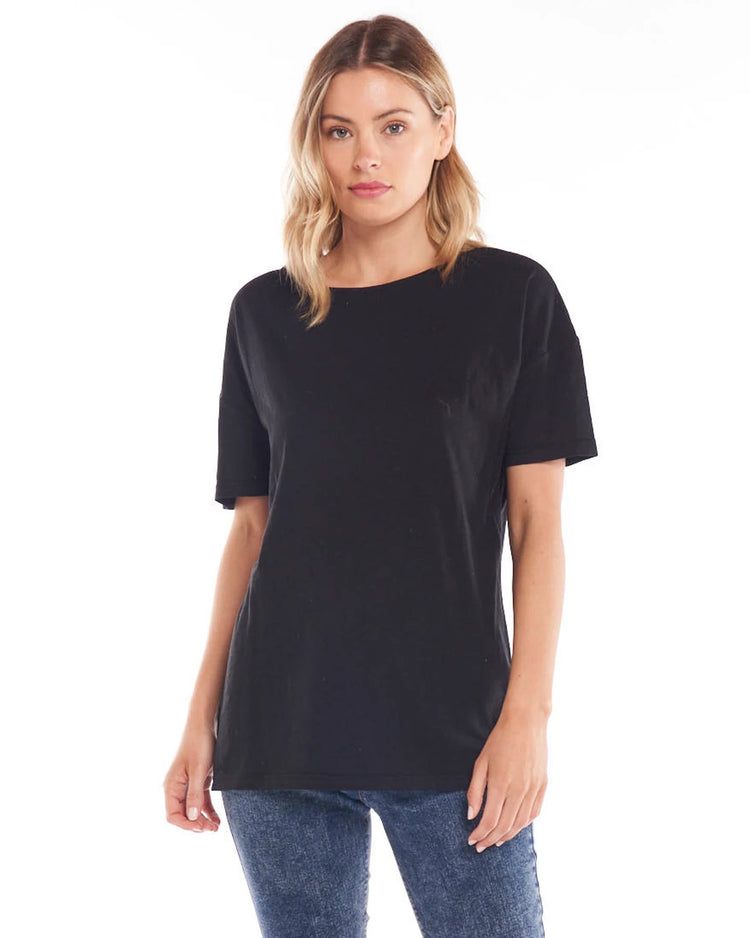 A female model wearing a black, Betty Basics relaxed fit t-shirt with a round neckline, short sleeves, and a side split detail.