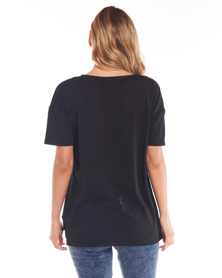 A female model wearing a black, Betty Basics relaxed fit t-shirt with a round neckline, short sleeves, and a side split detail.