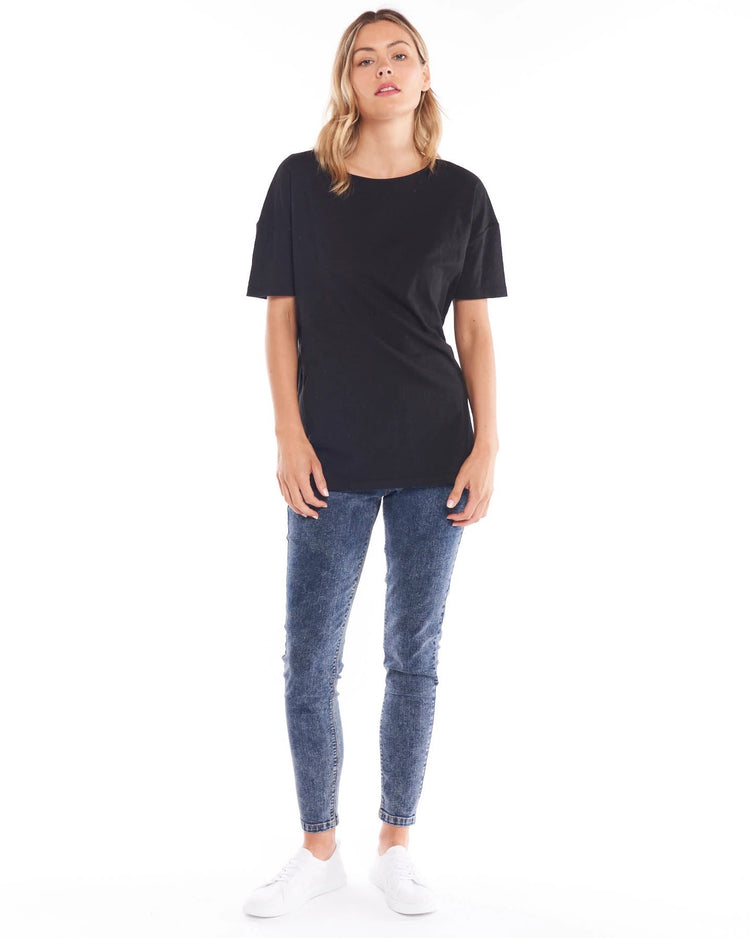 A female model wearing a black, Betty Basics relaxed fit t-shirt with a round neckline, short sleeves, and a side split detail.