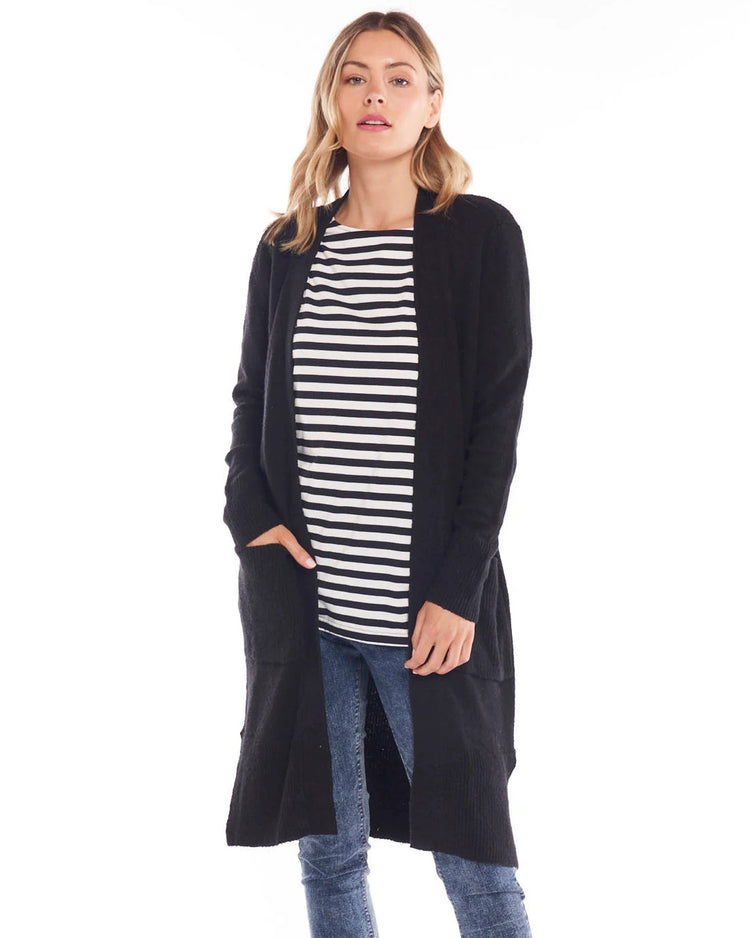 A female model wearing a long black cardigan with large patch pockets, over a striped top, paired with blue jeans.